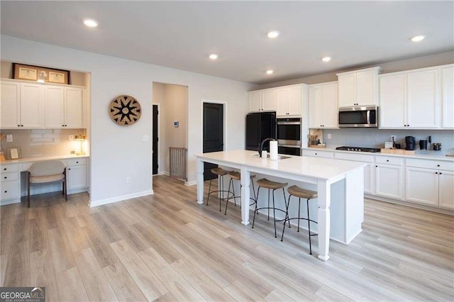 kitchen featuring white cabinets, built in desk, an island with sink, and black appliances