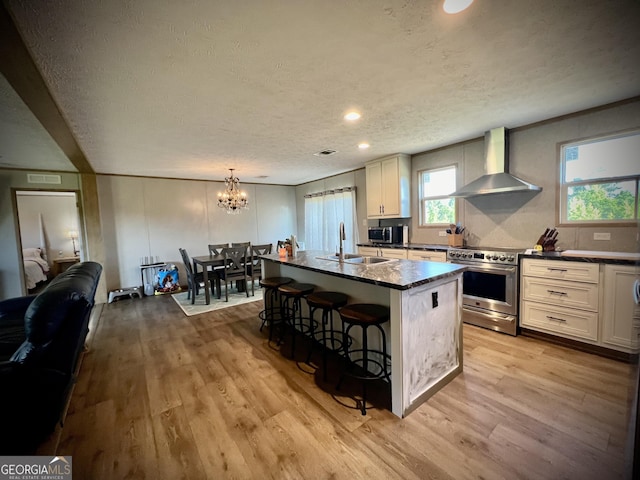 kitchen featuring stainless steel appliances, a textured ceiling, a kitchen bar, a kitchen island, and wall chimney range hood