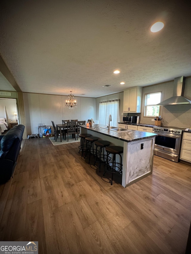 kitchen with a center island, stainless steel range with electric cooktop, wall chimney range hood, a kitchen breakfast bar, and sink