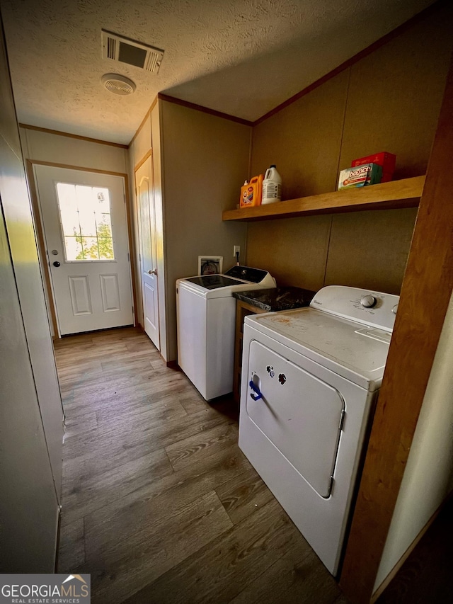 laundry area with crown molding, light wood-type flooring, washing machine and dryer, and a textured ceiling