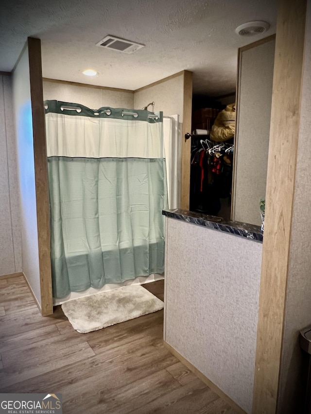 bathroom featuring wood-type flooring, a shower, and a textured ceiling