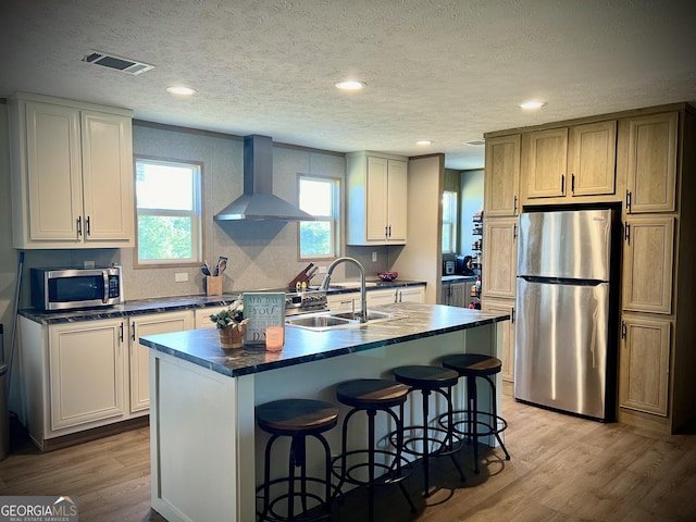 kitchen featuring wall chimney exhaust hood, light hardwood / wood-style flooring, stainless steel appliances, a center island with sink, and sink