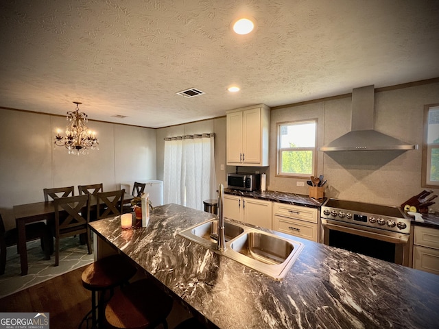 kitchen with a kitchen breakfast bar, stainless steel appliances, a textured ceiling, wall chimney exhaust hood, and sink