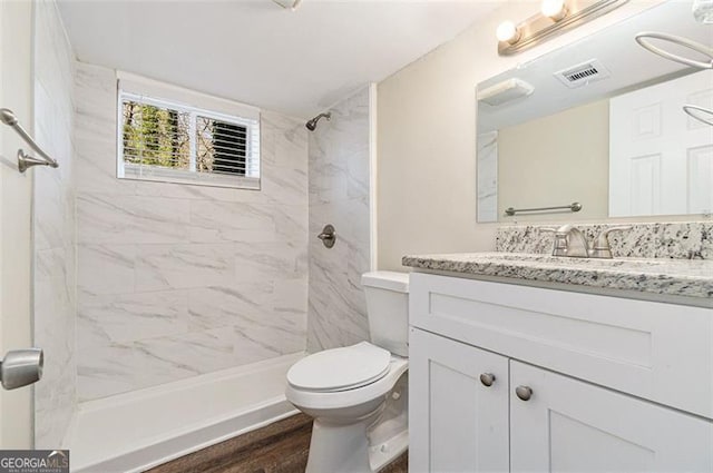 bathroom with hardwood / wood-style floors, a tile shower, vanity, and toilet