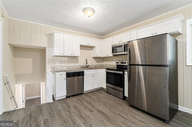 kitchen with light stone counters, sink, appliances with stainless steel finishes, and white cabinetry