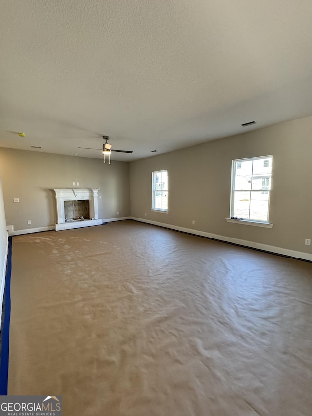 unfurnished living room with visible vents, a fireplace with raised hearth, a ceiling fan, a textured ceiling, and carpet flooring