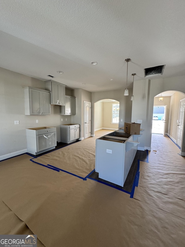 kitchen featuring arched walkways, a textured ceiling, carpet, and baseboards