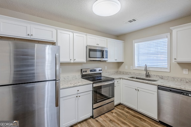 kitchen with sink, a textured ceiling, white cabinetry, light hardwood / wood-style floors, and appliances with stainless steel finishes