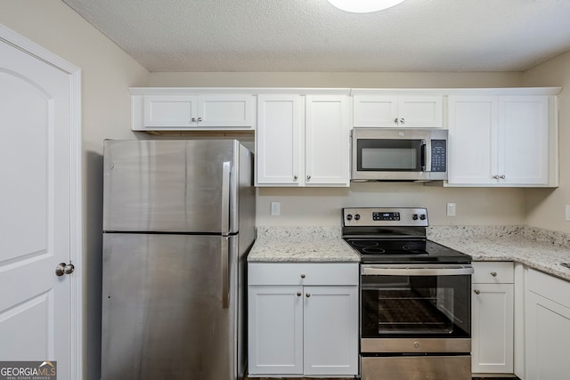 kitchen featuring stainless steel appliances, white cabinetry, a textured ceiling, and light stone counters