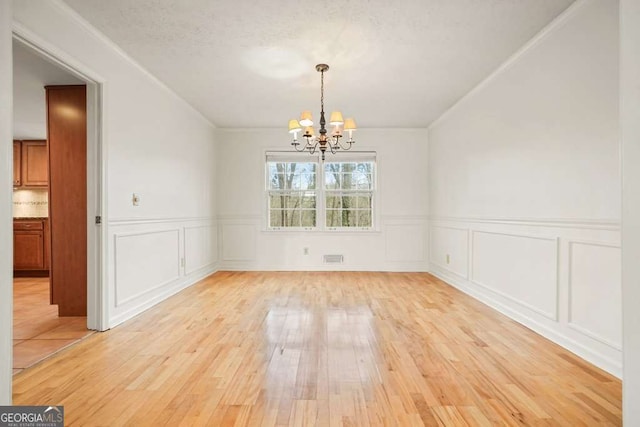 unfurnished dining area featuring light hardwood / wood-style flooring, crown molding, and a chandelier