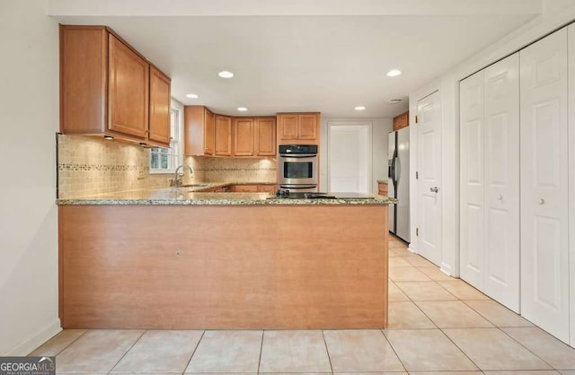 kitchen with sink, light stone counters, kitchen peninsula, and appliances with stainless steel finishes