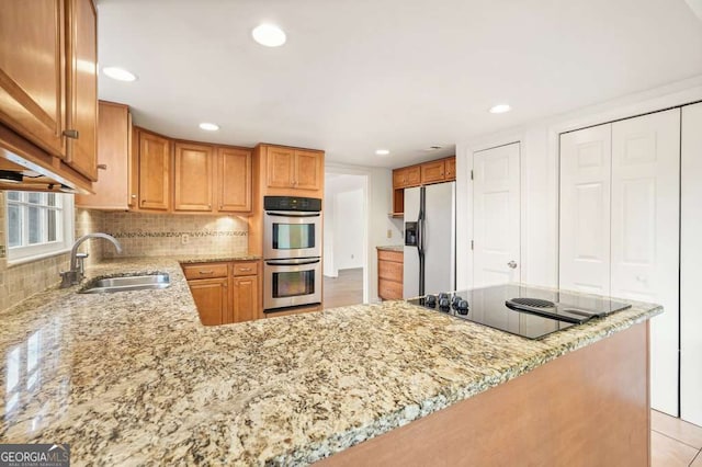 kitchen with stainless steel appliances, sink, light stone countertops, and kitchen peninsula