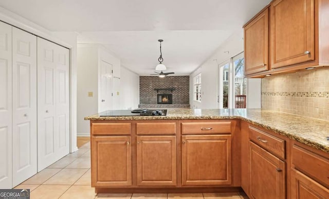 kitchen with black electric cooktop, kitchen peninsula, a brick fireplace, and decorative backsplash