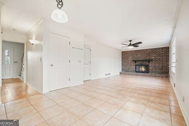 unfurnished living room with a fireplace, ceiling fan, light tile patterned floors, and crown molding