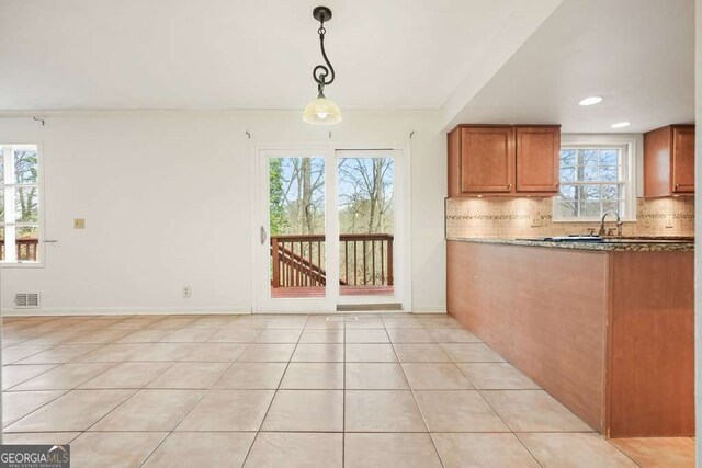 interior space featuring light tile patterned floors, tasteful backsplash, pendant lighting, and dark stone counters