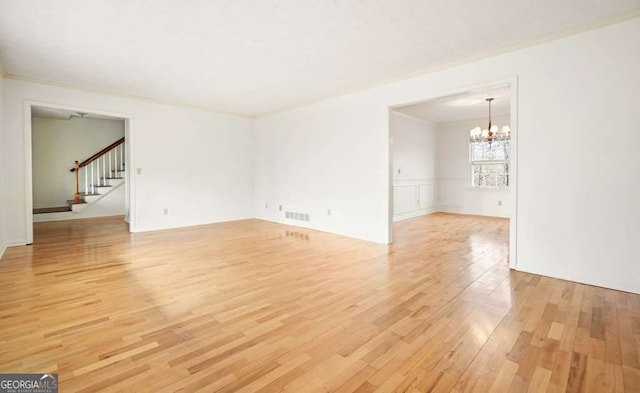 spare room featuring a notable chandelier, light hardwood / wood-style floors, and crown molding