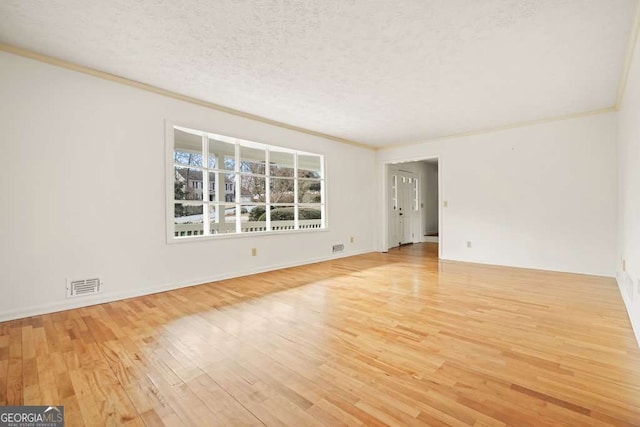 empty room featuring a textured ceiling, light wood-type flooring, and crown molding