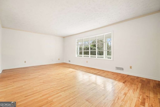 unfurnished room featuring a textured ceiling, light wood-type flooring, and crown molding