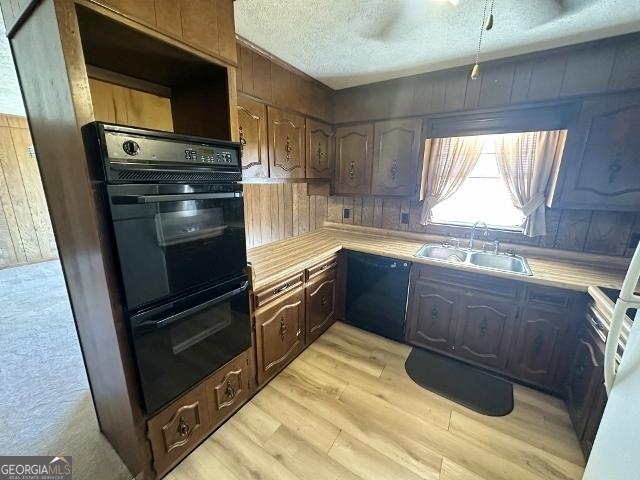 kitchen featuring sink, a textured ceiling, light hardwood / wood-style floors, wood walls, and black appliances