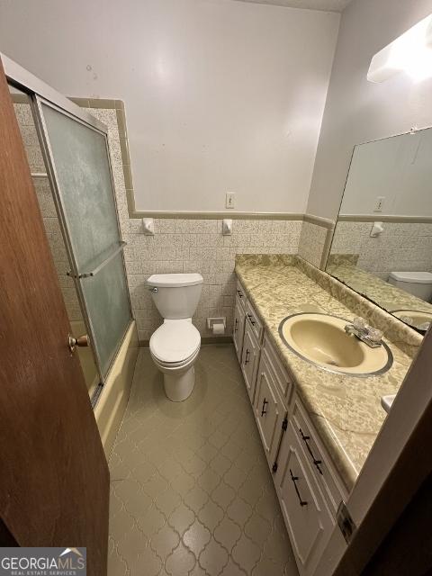 full bathroom featuring toilet, tile patterned flooring, tile walls, enclosed tub / shower combo, and vanity