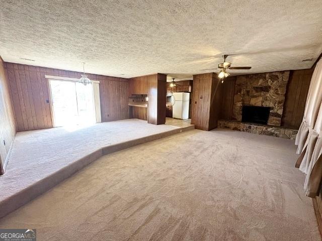 unfurnished living room with carpet floors, wood walls, ceiling fan, and a stone fireplace