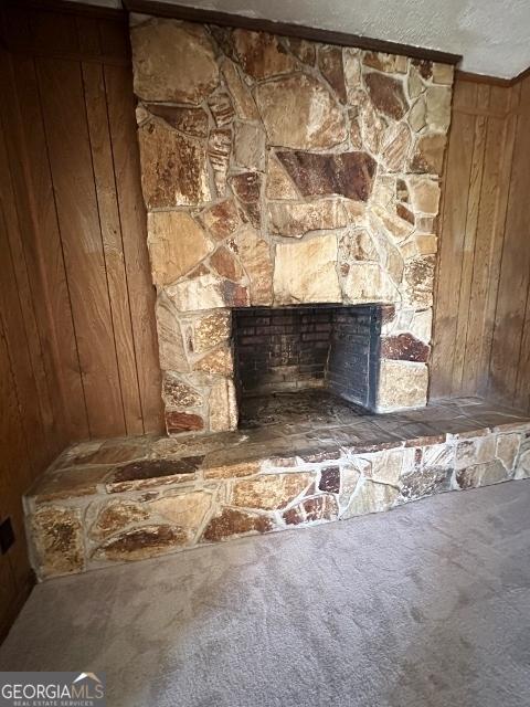 interior details featuring wooden walls, carpet floors, a textured ceiling, and a stone fireplace