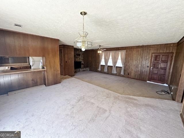 unfurnished living room featuring ceiling fan, light colored carpet, wooden walls, and a textured ceiling