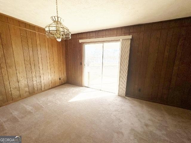 spare room featuring an inviting chandelier, wood walls, and carpet