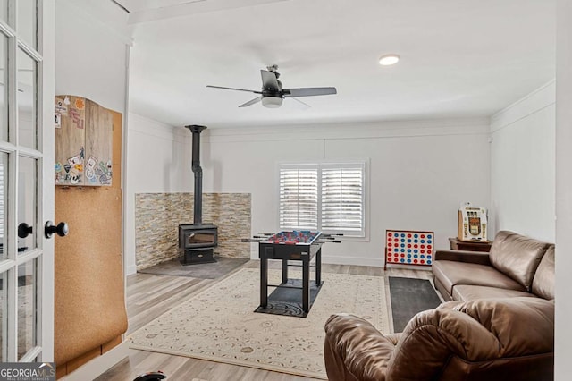 living room featuring ceiling fan, a wood stove, crown molding, and light wood-type flooring