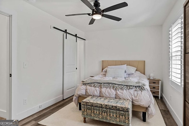 bedroom with ceiling fan, a barn door, and dark hardwood / wood-style floors