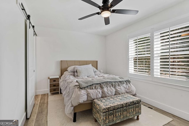 bedroom with light wood-type flooring, ceiling fan, and a barn door