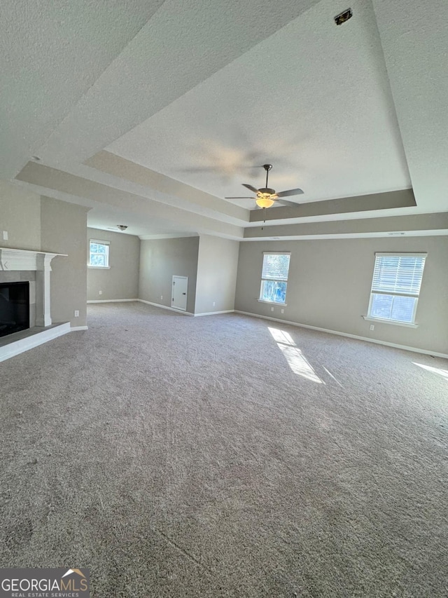 unfurnished living room with ceiling fan, carpet floors, a raised ceiling, and a textured ceiling