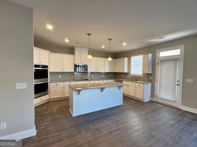 kitchen with light stone counters, a center island, stainless steel appliances, a breakfast bar area, and white cabinets