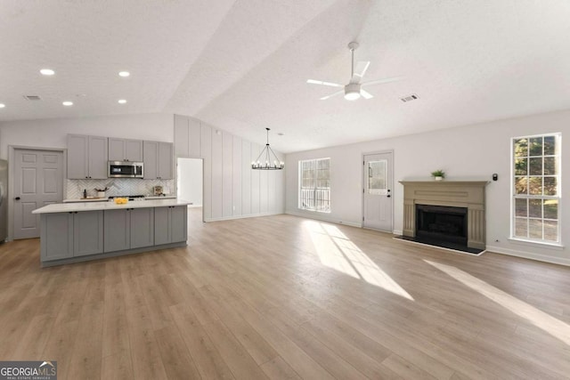 unfurnished living room featuring ceiling fan with notable chandelier, light hardwood / wood-style floors, a healthy amount of sunlight, and lofted ceiling