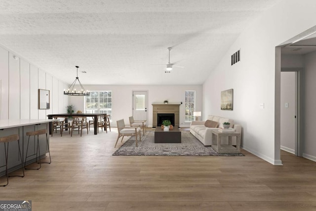 living room featuring a textured ceiling, hardwood / wood-style floors, lofted ceiling, and ceiling fan with notable chandelier