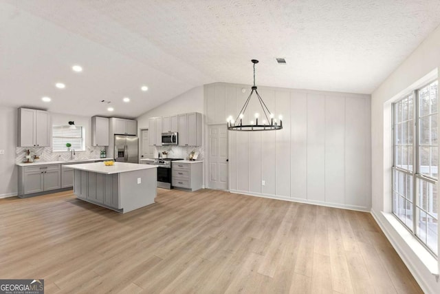 kitchen with decorative light fixtures, stainless steel appliances, lofted ceiling, a kitchen island, and gray cabinetry