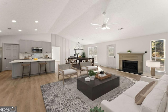 living room with ceiling fan with notable chandelier, vaulted ceiling, light hardwood / wood-style flooring, and a wealth of natural light