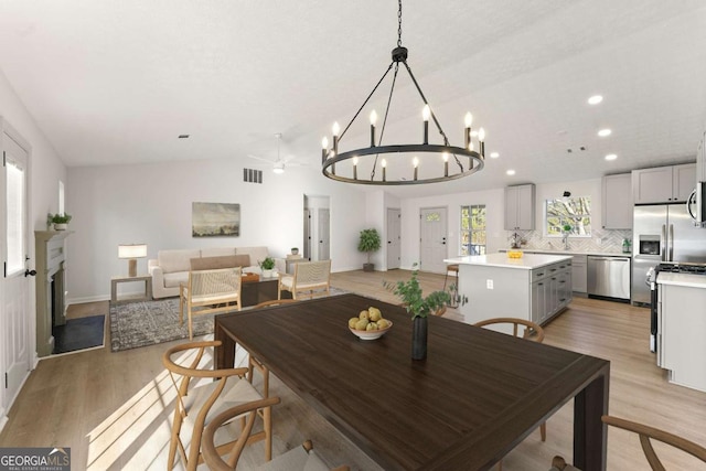 dining area featuring light hardwood / wood-style floors, sink, lofted ceiling, and ceiling fan with notable chandelier