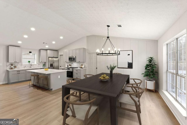 dining space featuring a textured ceiling, lofted ceiling, light wood-type flooring, an inviting chandelier, and sink