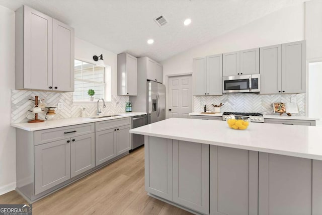 kitchen featuring stainless steel appliances, sink, lofted ceiling, light wood-type flooring, and gray cabinetry