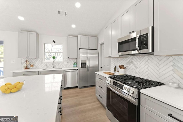 kitchen with stainless steel appliances, sink, a textured ceiling, light hardwood / wood-style flooring, and decorative backsplash