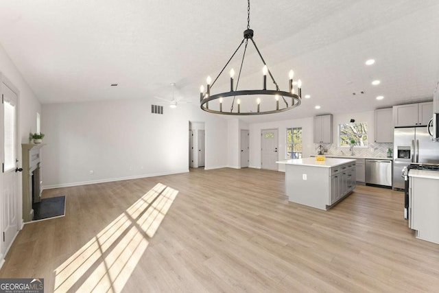 kitchen with vaulted ceiling, gray cabinets, stainless steel appliances, a kitchen island, and backsplash