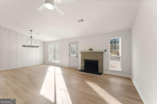 unfurnished living room with a textured ceiling, light hardwood / wood-style flooring, and ceiling fan with notable chandelier