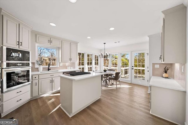 kitchen featuring decorative light fixtures, a center island, wood-type flooring, decorative backsplash, and stainless steel gas stovetop