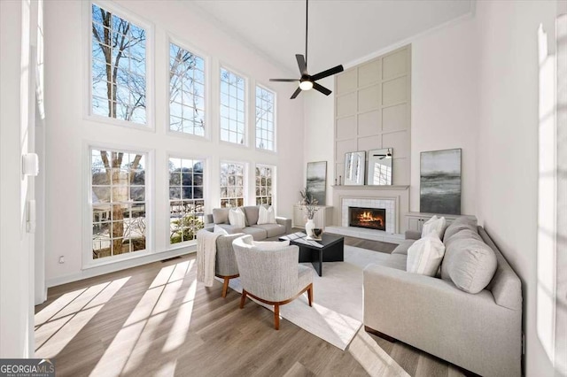 living room featuring ceiling fan, light hardwood / wood-style flooring, a fireplace, and a high ceiling