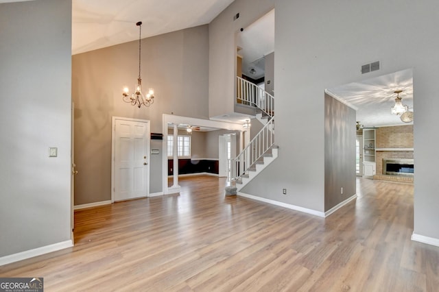 entryway with ceiling fan with notable chandelier, a fireplace, a towering ceiling, and light hardwood / wood-style flooring