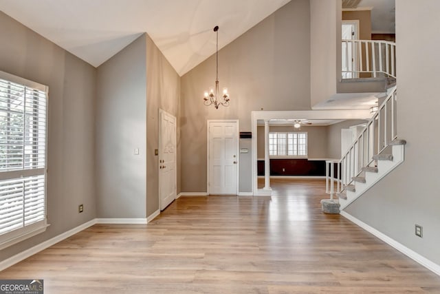 foyer with ceiling fan with notable chandelier, high vaulted ceiling, and light hardwood / wood-style flooring