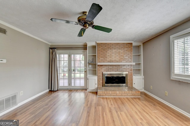 unfurnished living room with a brick fireplace, a textured ceiling, light hardwood / wood-style floors, and built in features