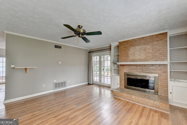 unfurnished living room featuring a textured ceiling, a fireplace, ornamental molding, ceiling fan, and light wood-type flooring