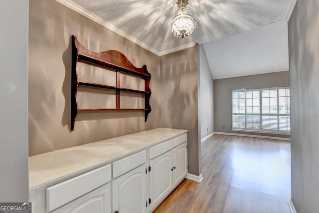 interior space featuring a textured ceiling, a chandelier, light hardwood / wood-style floors, crown molding, and white cabinetry